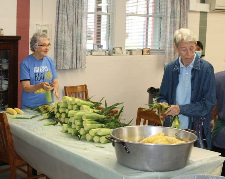 Sister Ann Patrice Cecil, left, and Sister Maureen O’Neill shuck the corn and place it in a tub.