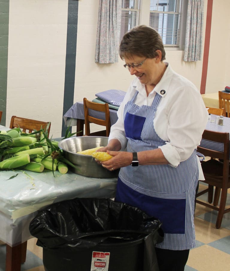 Sister Amelia Stenger keeps a smile on her face as she cleans the corn of its silks.