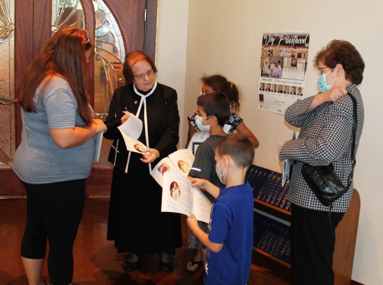 Sister Rosanne shows some parishioners of Precious Blood Church her photo in the worship aide created for Mass.
