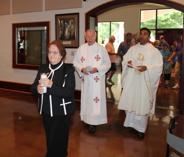 Sister Rosanne carries a candle as part of the opening procession, leading Father Ed Bradley, left, and Father Suneesh Mathew, the pastor of Precious Blood.