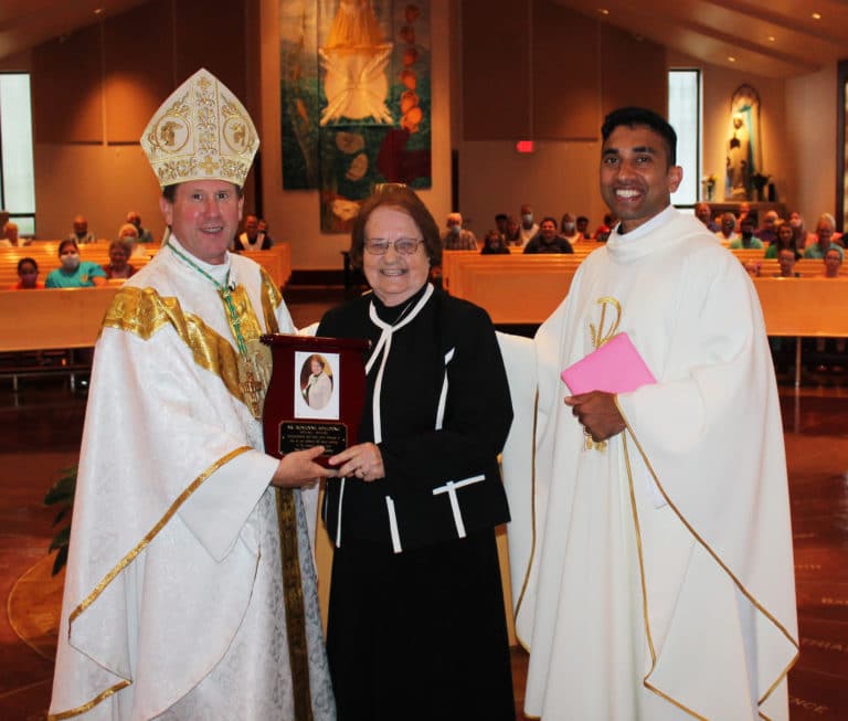 Bishop Mark Spalding, left, and Father Suneesh Mathew, present Sister Rosanne a plaque honoring her for her 60 years of service as an Ursuline Sister.