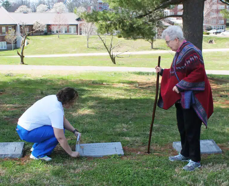 Sagan Storm, left, of Brescia University, plants a flag on the grave of Sister Fran Wilhelm, who created the Centro Latino ministry in Daviess County. Sister Michele Morek looks on, and told Storm that Sister Fran was the first Ursuline Sister she met, while attending elementary school in New Mexico. Sagan Storm, left, of Brescia University, plants a flag on the grave of Sister Fran Wilhelm, who created the Centro Latino ministry in Daviess County. Sister Michele Morek looks on, and told Storm that Sister Fran was the first Ursuline Sister she met, while attending elementary school in New Mexico.