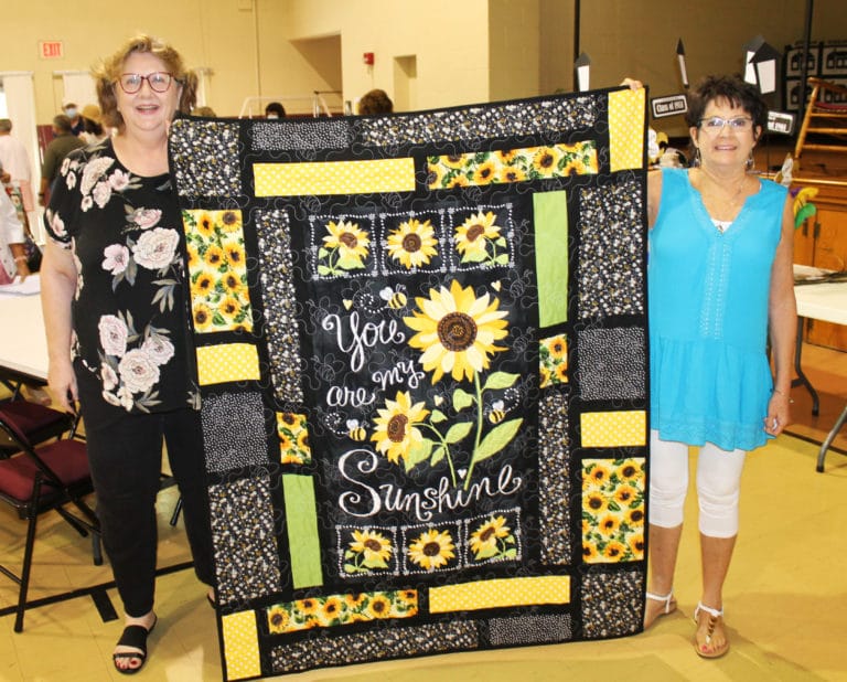 Maryann Clements Carr, A72, left, holds up the wall hanging she won, which was created by Karen Calhoun McCarty, A74, right.