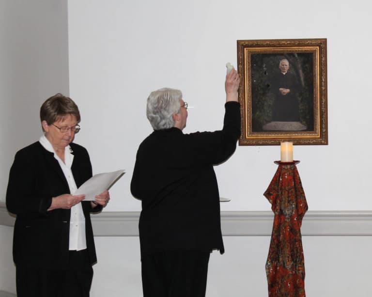 Sister Pat Lynch, right, assistant congregational leader, blesses the portrait of Father Volk with holy water. Sister Amelia Stenger, left, congregational leader, read a pray for Father Volk.