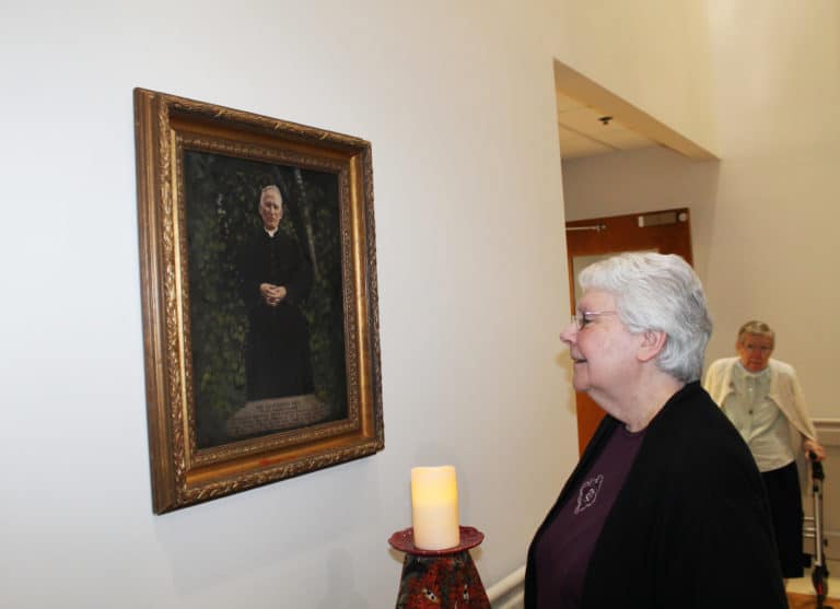 Sister Pat Lynch, assistant congregational leader, reads the information on the portrait about Father Volk after the prayer service. At right is Sister Amanda Rose Mahoney.