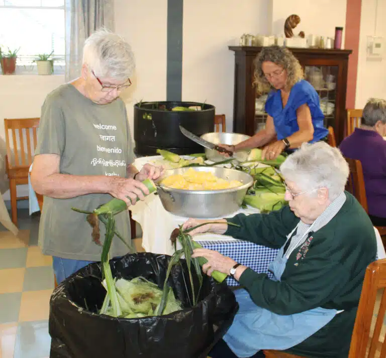 Sister Jane Falke, left, and Sister Michael Ann Monaghan, seated, shuck their corn, as Ashley Wilkerson, coordinator of pastoral care and activities in Saint Joseph Villa, wields a big knife in the background. Sister Jane Falke, left, and Sister Michael Ann Monaghan, seated, shuck their corn, as Ashley Wilkerson, coordinator of pastoral care and activities in Saint Joseph Villa, wields a big knife in the background.