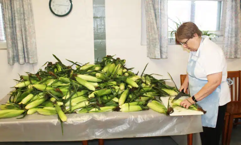 Sister Amelia Stenger chops the ends off a table full of corn to get them ready for shucking. Sister Amelia Stenger chops the ends off a table full of corn to get them ready for shucking.