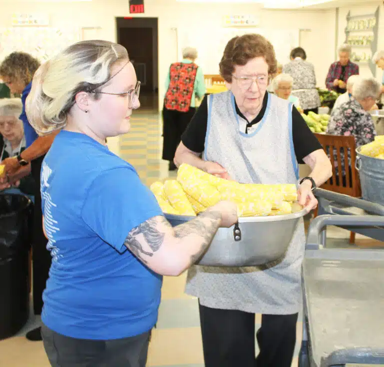Bailey Tipton, left, a member of the Food Service staff, assists Sister Mary Henning in loading a full pan of corn to a rolling cart. Bailey Tipton, left, a member of the Food Service staff, assists Sister Mary Henning in loading a full pan of corn to a rolling cart.