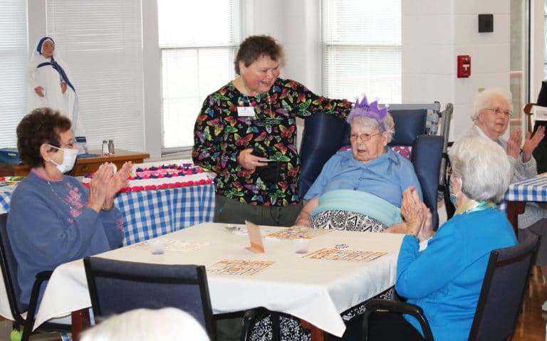 Sister Alicia Coomes, standing, the coordinator of pastoral care for the Sisters in Saint Joseph Villa, leads the singing of “Happy Birthday” for Sister Marie and Sister Elaine, right. Clapping at left is Sister Susan Mary Mudd.