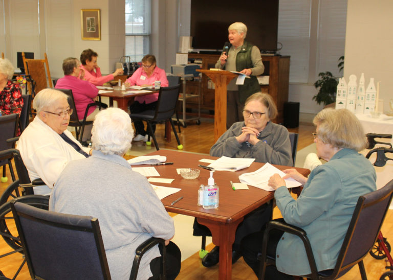 Sister Suzanne Sims, in the background, addresses the Sisters. Conversation at this table involves, from left, Sister Sara Marie Gomez, Sister Ann McGrew, Sister Lois Lindle and Sister Catherine Barber.