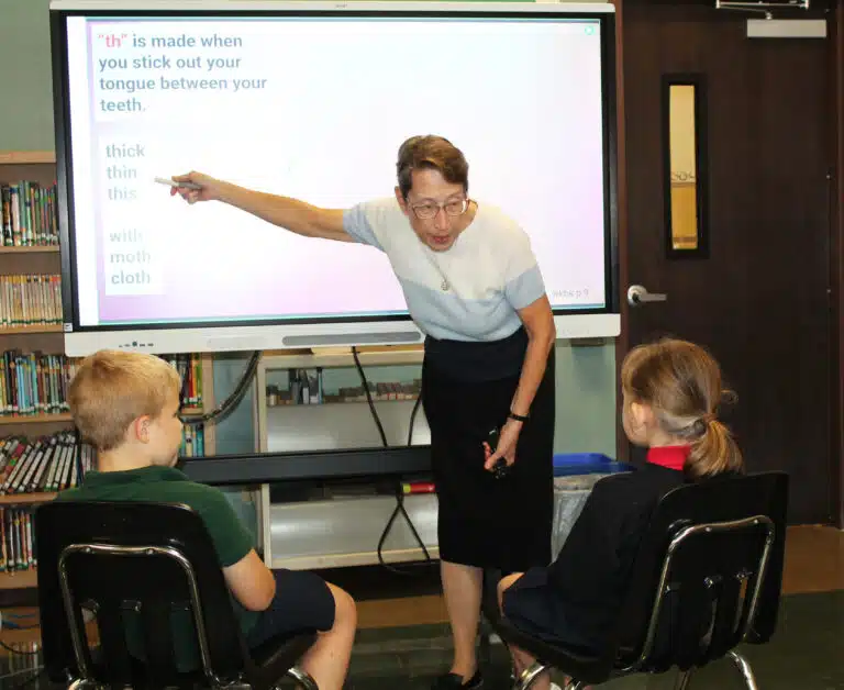 Sister Marilyn Mueth uses the Smart board to work on a vocabulary lesson for two second-grade students. Sister Marilyn Mueth uses the Smart board to work on a vocabulary lesson for two second-grade students.