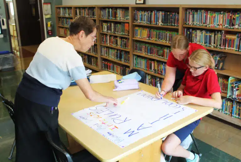 During a seventh-grade math flex class, Sister Marilyn Mueth assists these girls working on a poster. During a seventh-grade math flex class, Sister Marilyn Mueth assists these girls working on a poster.