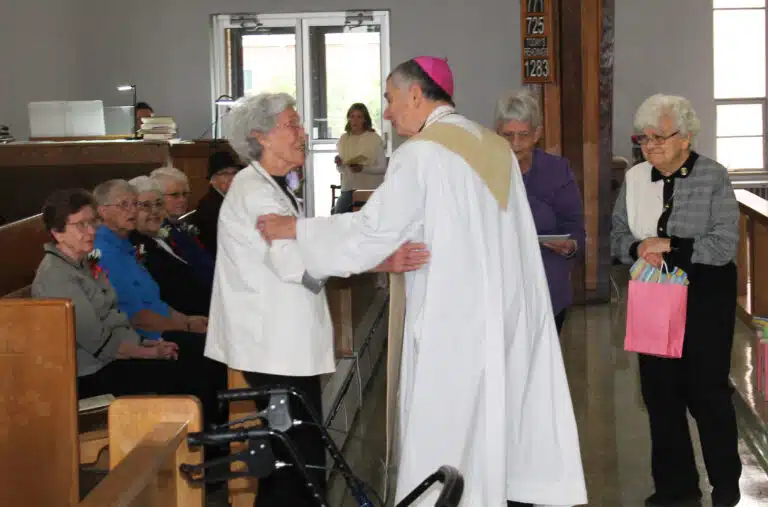 Each sister is called up one at a time to receive a certificate, a gift, and congratulations from Bishop Medley. Here Sister Elaine Burke is congratulated by the bishop, as Ursuline Sister Cecelia Joseph Olinger, right, prepares to hand her a gift, and Ursuline Sister Mary Celine Weidenbenner readies her certificate. Each sister is called up one at a time to receive a certificate, a gift, and congratulations from Bishop Medley. Here Sister Elaine Burke is congratulated by the bishop, as Ursuline Sister Cecelia Joseph Olinger, right, prepares to hand her a gift, and Ursuline Sister Mary Celine Weidenbenner readies her certificate.