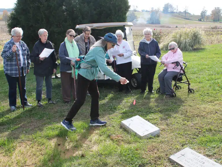 Kathryn McSorley sprinkles holy water on Sister Sheila Anne’s grave, as the Sisters look on.