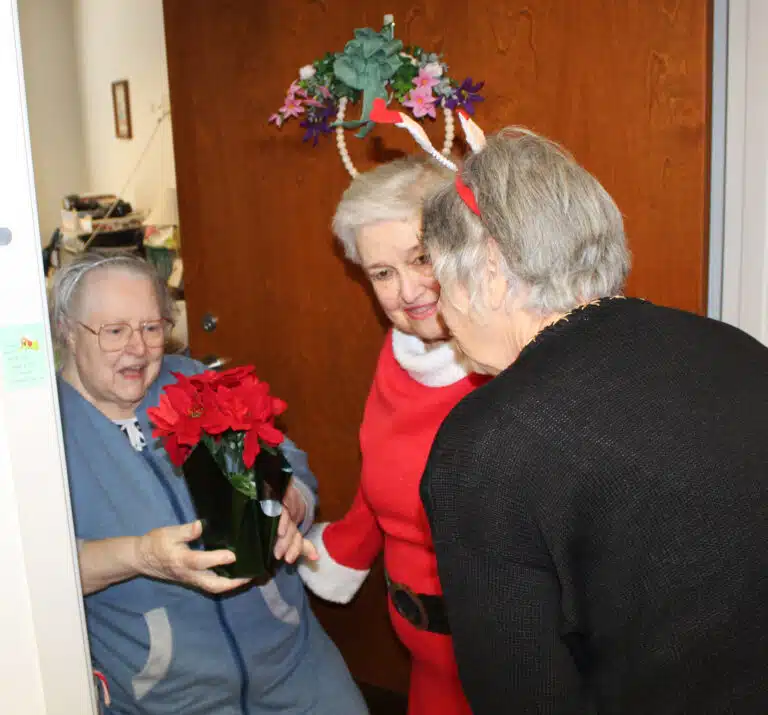 Sister Catherine Marie Lauterwasser holds her poinsettia as she talks with Elaine Wood and Sid Mason. Sister Catherine Marie Lauterwasser holds her poinsettia as she talks with Elaine Wood and Sid Mason.