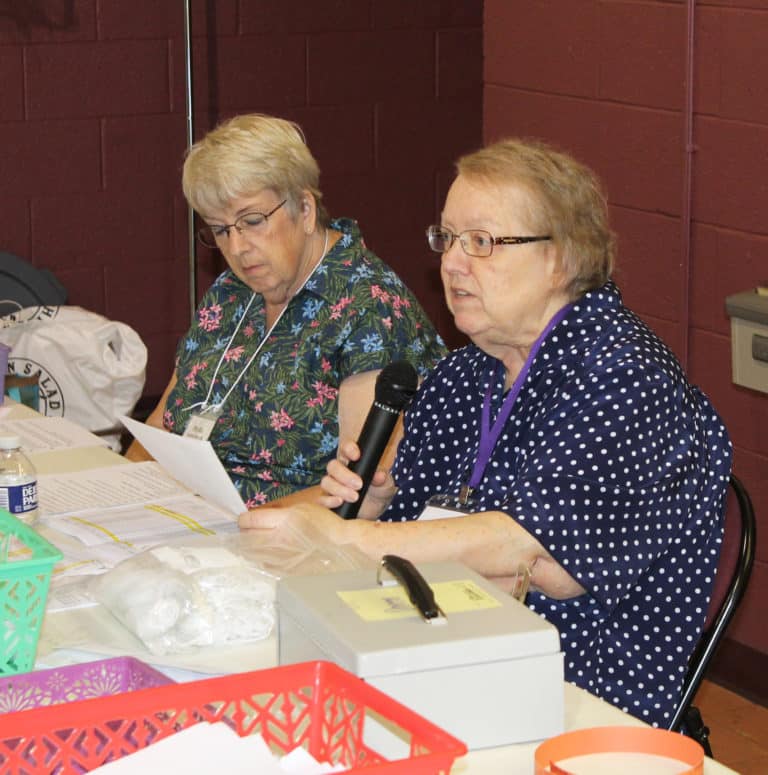 Mary Costello A’65, right, reads a reflection she read for the opening prayer, as her sister, Phyllis Bresnik, follows along. The Costello sisters come from California every year and handle the registration table.