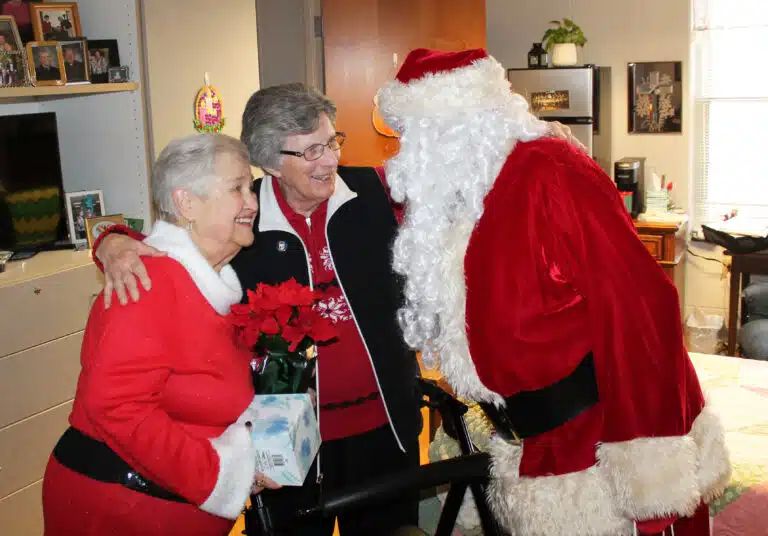 Sister Margaret Ann Aull hugs Santa and Mrs. Claus like they are old friends.