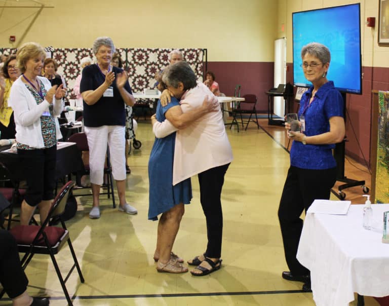 Sister Cheryl Clemons, right, hugs Mary Margaret Drury after reading her nomination for the Maple Leaf Award. Applauding at left are Susan Thomas Allgeier and Cecilia Robinette McEldowney, with Stephanie Warren at right.