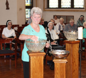 Sister Pam Mueller places her lighted candle in the bowl of water. This year, Sister Pam celebrates 50 years since she graduated from the Academy.