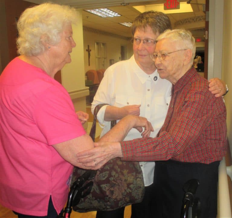 Sister Amelia Stenger drapes an arm around Sister Marie Bosco Wathen as they talk with Sister Vivian Bowles.