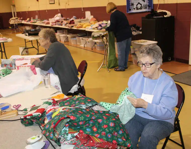 Pat Strittmatter works on a bib as her friend Associate Mary Teder, left, hand quilts her project.