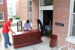 Movers roll a desk out of the building onto the porch, and prepare to load it on a truck to move to Lourdes Hall. The Ursuline leadership Council had their offices in St. Angela Hall beginning in 1950. The upper two floors were residences for sisters.