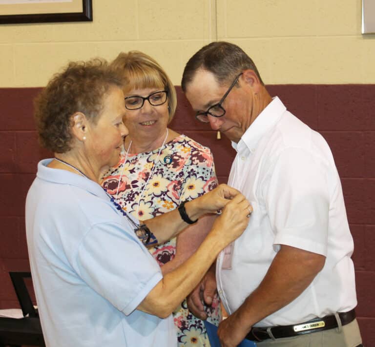 Sister Alicia Coomes pins Jamie Durbin following his commitment as an Associate, as his wife Alice smiles.