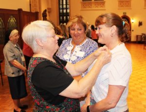 Sister Suzanne Sims places an Associate pin on Doreen Abbott, as Martha Warren awaits hers.