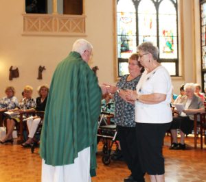 Associates Marilyn Katzer, left, and Mary Ann Stewart present the offertory gifts to Father Joe Mills.