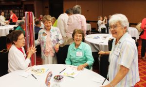Sister Mary Henning, left, Sister Elaine Burke, second from right, and Sister Cecelia Joseph Olinger, right, all Ursulines of Mount Saint Joseph, join Sister Julia Davis, an Ursuline of Louisville, prior to the opening prayer July 7. Sister Julia was one of the pole carriers leading the sisters of each community to the front of the room during the opening ceremony.