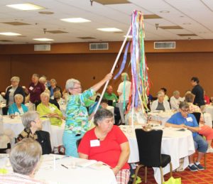 Sister Pam Mueller, of Mount Saint Joseph, carries the brightly colored pole of ribbons as she leads the Ursuline Sisters of Tildonk to the front of the room with their lighted candles.