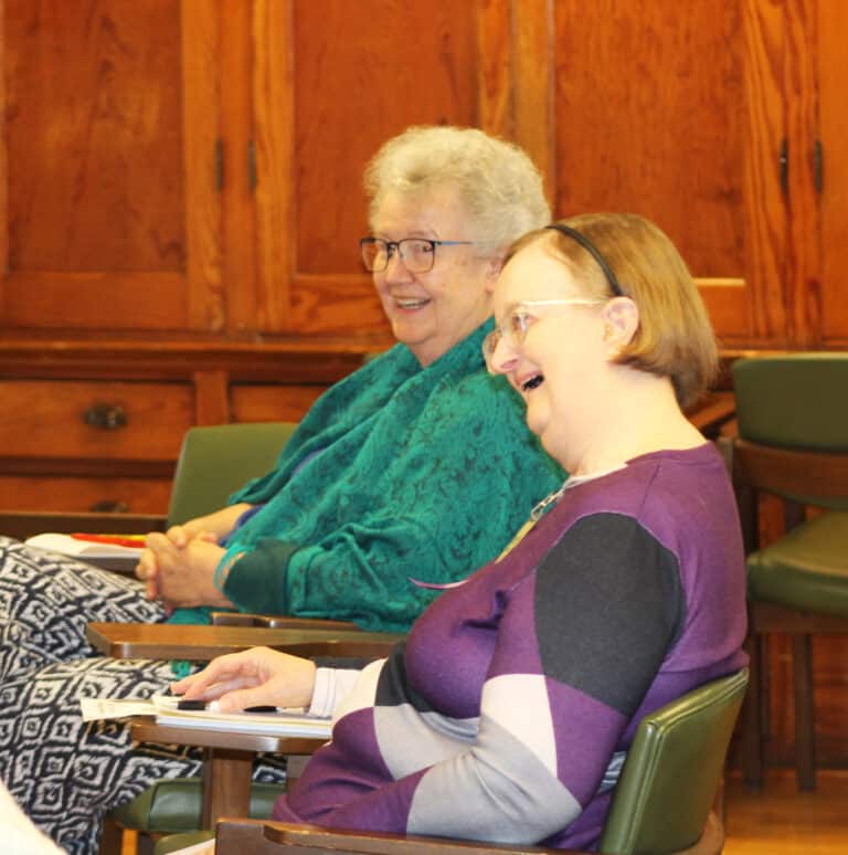 Sister Michele Morek, left, and Sister Rebecca White share a laugh during part of the presentation. Sister Michele said she was most affected by a drawing that said, “windmills not weapons.” She recalled a song lyric that asked what could be done with all the money that is spent on wars.