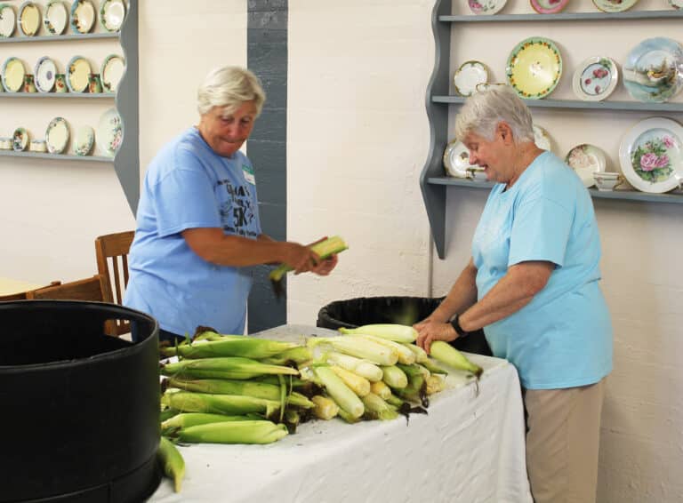 Sister Suzanne Sims, right, is joined by her sister, Teresa “T” Edwards as they cut ears of corn.