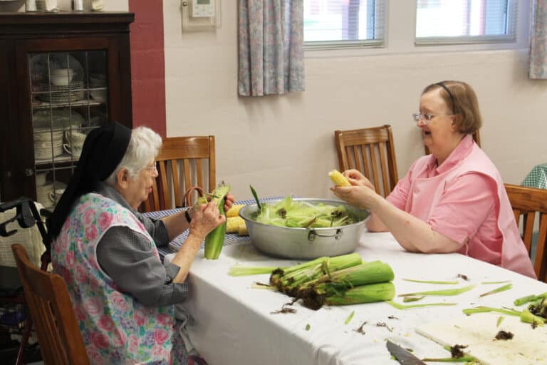 Sister Rebecca White, right, talks with Sister Michael Ann Monaghan as they strip their corn.
