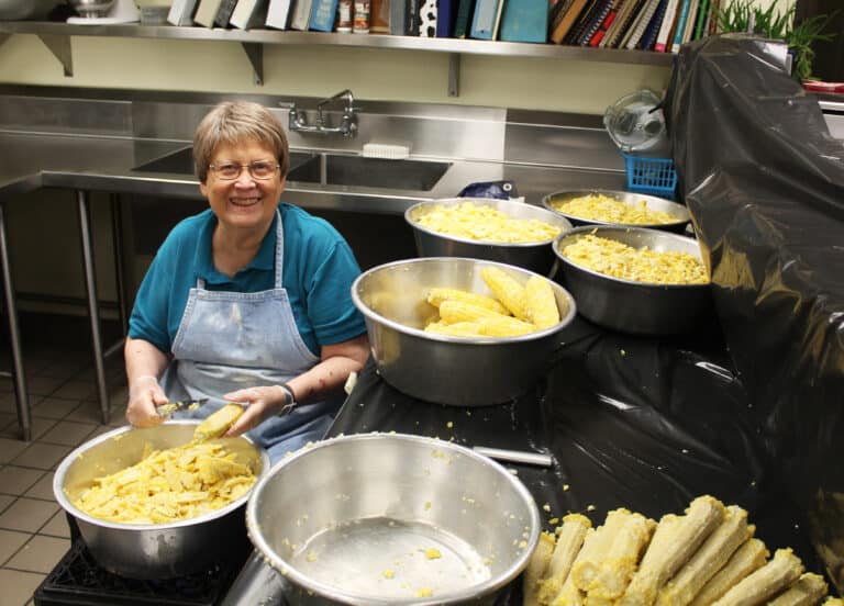 Sister Amelia Stenger sits among just a few of the pans of corn she cut off the cob on Aug. 1.