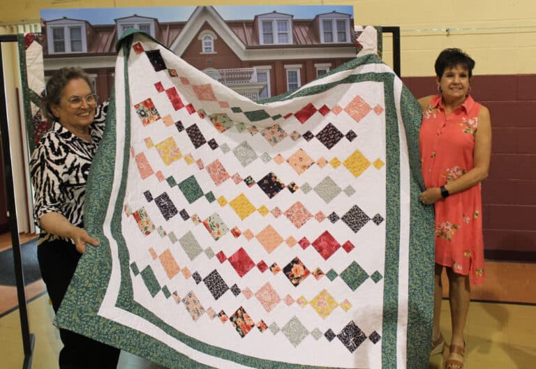 Mary Lou Byrne Payne A’66, left, holds the quilt she won that was made by Karen Calhoun McCarty A’74, right.