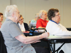 Sister Mary Agnes VonderHaar, left, and Sister Paul Marie Greenwell listen as Father Conley equates a line from “Hello Dolly” to how we deal with grief.