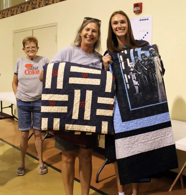 Kenna Newsome of Lewisport, right, originally chose the “Lots of Stripes” quilt that her Mom, Jeanne Chancellor, is holding, but she changed her mind after seeing the “Wars in the Stars No More” quilt. Her mother wanted the other quilt, so she purchased it. Kenna’s aunt, Peggy Duncan, is standing in the background. Kenna Newsome of Lewisport, right, originally chose the “Lots of Stripes” quilt that her Mom, Jeanne Chancellor, is holding, but she changed her mind after seeing the “Wars in the Stars No More” quilt. Her mother wanted the other quilt, so she purchased it. Kenna’s aunt, Peggy Duncan, is standing in the background.