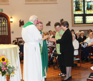Sister Amelia Stenger, right, and Sister Sharon Sullivan present the offertory gifts to Bishop William Medley and Father Ray Goetz.