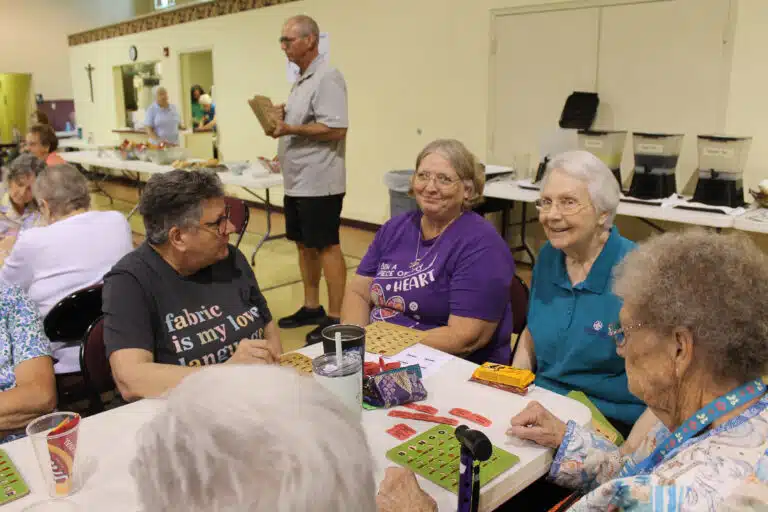 Ann Jacobs, wearing purple, smiles as she plays quilt bingo. She is Sister Amelia Stenger’s niece. At left is Carin Oliver, and at right is Sister Pat Lynch, who was volunteering at her first Quilt Bingo (she previously lived in Kansas). Ann Jacobs, wearing purple, smiles as she plays quilt bingo. She is Sister Amelia Stenger’s niece. At left is Carin Oliver, and at right is Sister Pat Lynch, who was volunteering at her first Quilt Bingo (she previously lived in Kansas).