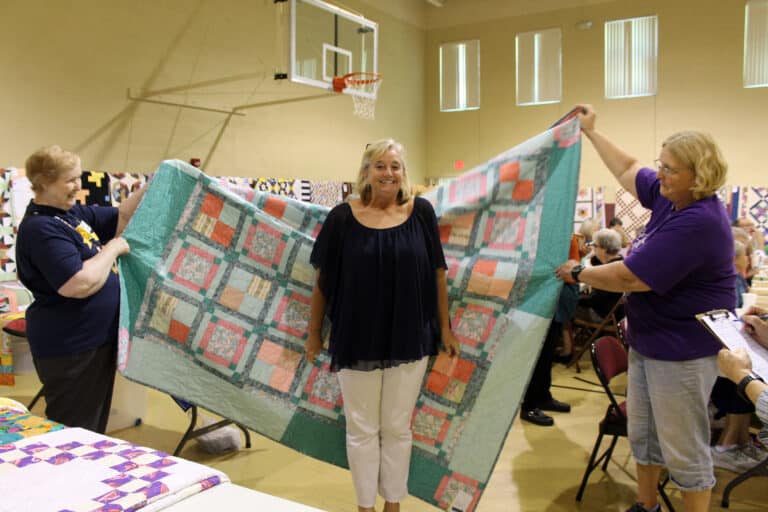 Kaye Fulkerson of Utica, Ky., smiles after winning the first quilt in Quilt Bingo. The quilt is being held up by Sister Helena Fischer, left, and Ann Jacobs, Sister Amelia Stenger’s niece. The quilt was called “Spring Fling.”