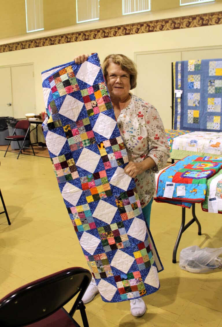 Anne Alexander of Owensboro is almost covered up by her new “Scrappy Stars” quilt.