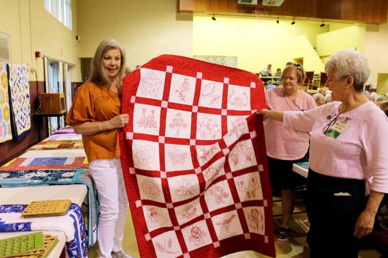 Gwen Howard of Whitesville, Ky., was happy to win the red “Flaming Flowers” quilt. Sister Pam Mueller, right, helps hold it up.