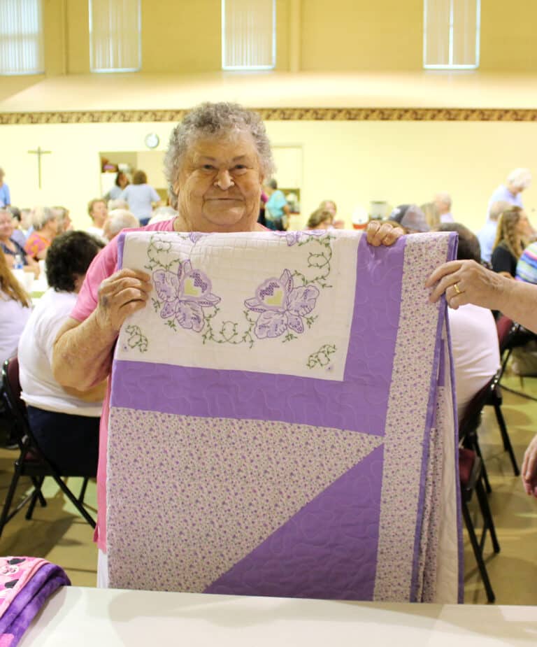 Mary Fleming of Morgantown, Ky., carries her new “Lovely Lavender” quilt that she won.