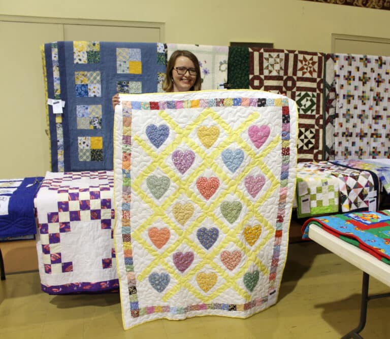 Molly Eby of Bloomfield, Ky., smiles as she holds up the “Baby Love” quilt she picked out after winning a round of bingo.