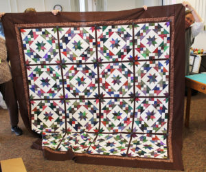 The quilters took a break on Feb. 22 for “show and tell,” so they could admire Scrap Happy, this quilt top completed by Eloise Hughes to be part of the next Quilt of the Month club. Sister Amelia Stenger is peeking out from the right.