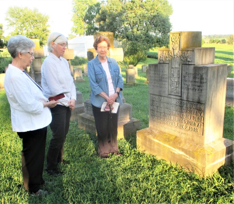 Sister Nancy Murphy, left, Sister Nancy Liddy, center, and Sister Mary Henning gather in front of the tombstone of Father Paul Volk, the priest who brought the Ursuline Sisters to what is now Maple Mount in 1874. Father Volk supported the Sisters in becoming an independent community.