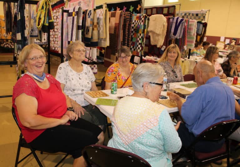 Ann Jacobs, left, shares a laugh between bingo games. She and her mother, Associate Mary Teder, next to her, helped put up many of the quilts that were available. They are joined at right by Associates John and Elaine Wood, and to their left by Sally Fitzgerald, who made several of the quilts, and Dee Dee Jackson,.