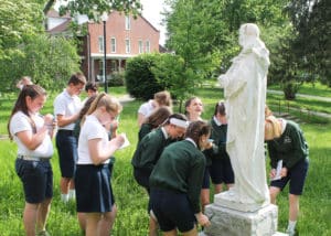 Students gather in front of the Saint Agnes statue to learn about the patron saint of young girls. The Guest House is in the background.