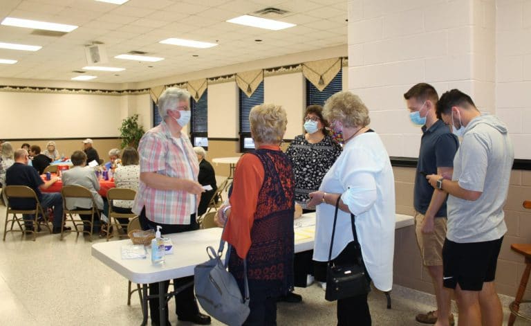 Sister Mary Timothy Bland, standing at left, helps Ursuline Associates Carol Hill, second from left, and Suzanne Reiss, check in. Associate Martha Alle, standing behind the table, was selling raffle tickets.